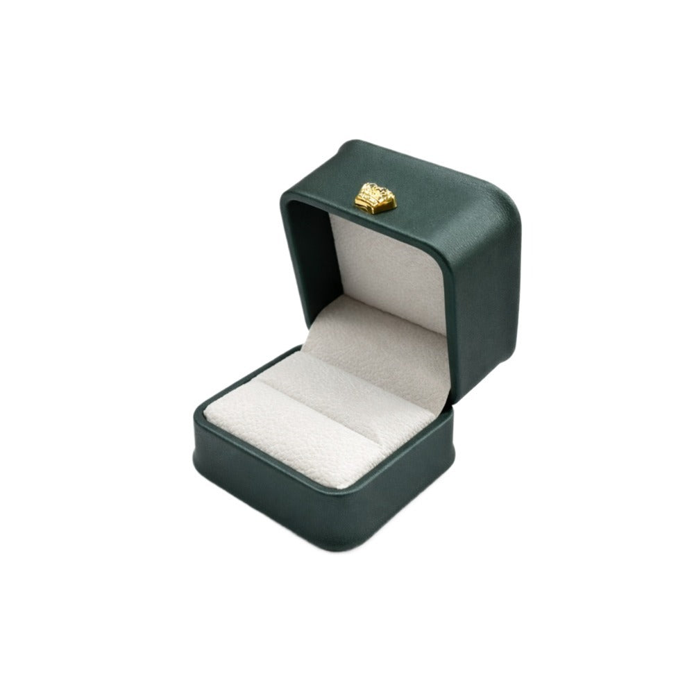 Open emerald green rounded-corner ring case with a light cushioned insert and gold-tone ornament.