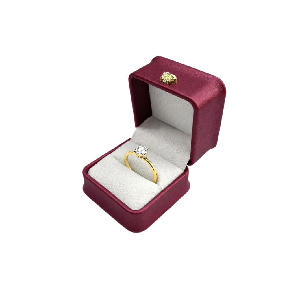 Open burgundy rounded-corner ring box displaying a gold engagement ring in the light padded insert.